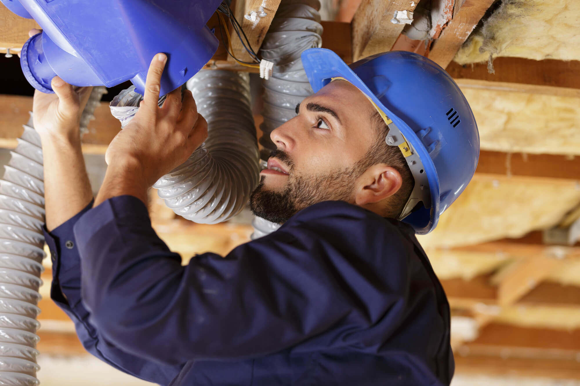 Young male worker installing air conditioning unit into roof